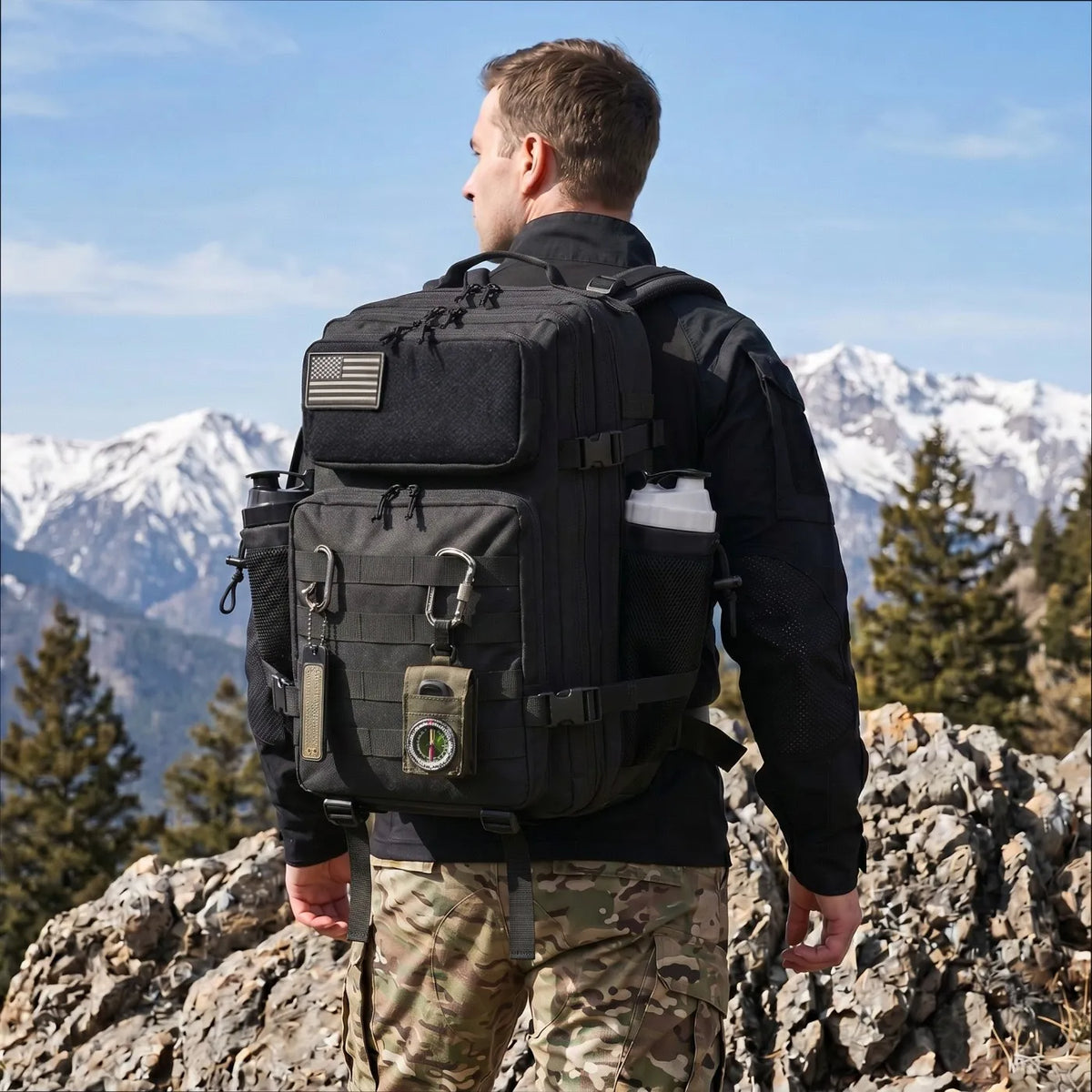 Sort taktisk rygsæk med MOLLE-stropper, lommer og påsat lille amerikansk flag båret på ryggen af en mand i bjergene.