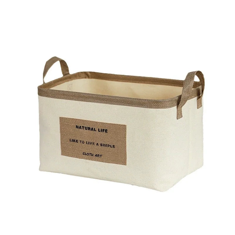 Rektangulær beige stofkurv med brune hanke og tekstmærke på forsiden.