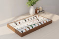 Brun bakke i træ med 30 rum med lyse puder, fyldt med armbåndsure og smykker.