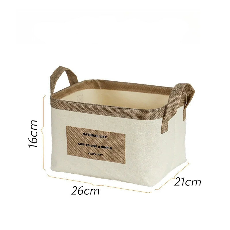 Rektangulær beige stofkurv med brune hanken og et tekstmærke foran. Mål: 26x21x16 cm.
