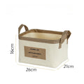 Rektangulær beige stofkurv med brune hanken og et tekstmærke foran. Mål: 26x21x16 cm.