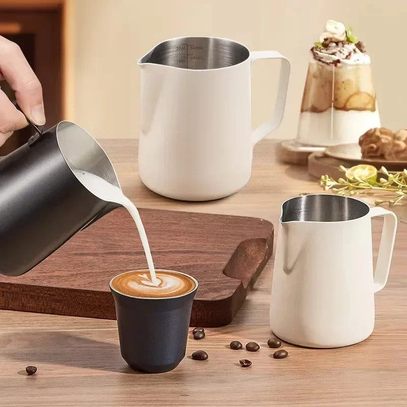 To mælkekander i hvid og en sort, der hælder mælk i en kop med kaffe.