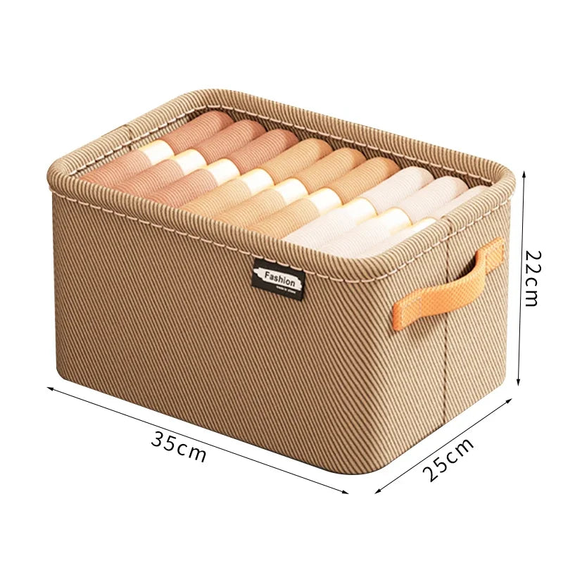 Beige opbevaringskasse i stof med håndtag og rullede tekstiler indeni. Mål: 35x25x22 cm.